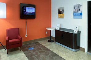 A reception area with a red chair, a TV mounted on the wall, a small table, and a cabinet with a sign.