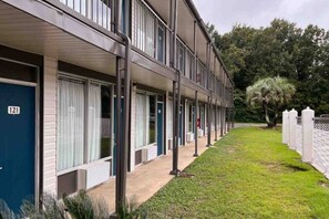 A row of motel rooms with a number '121' visible, a covered walkway, and a fenced area with trees.
