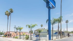 Ein Motel mit einem blauen Schild, das kostenloses WLAN anzeigt, umgeben von Palmen und blauem Himmel.