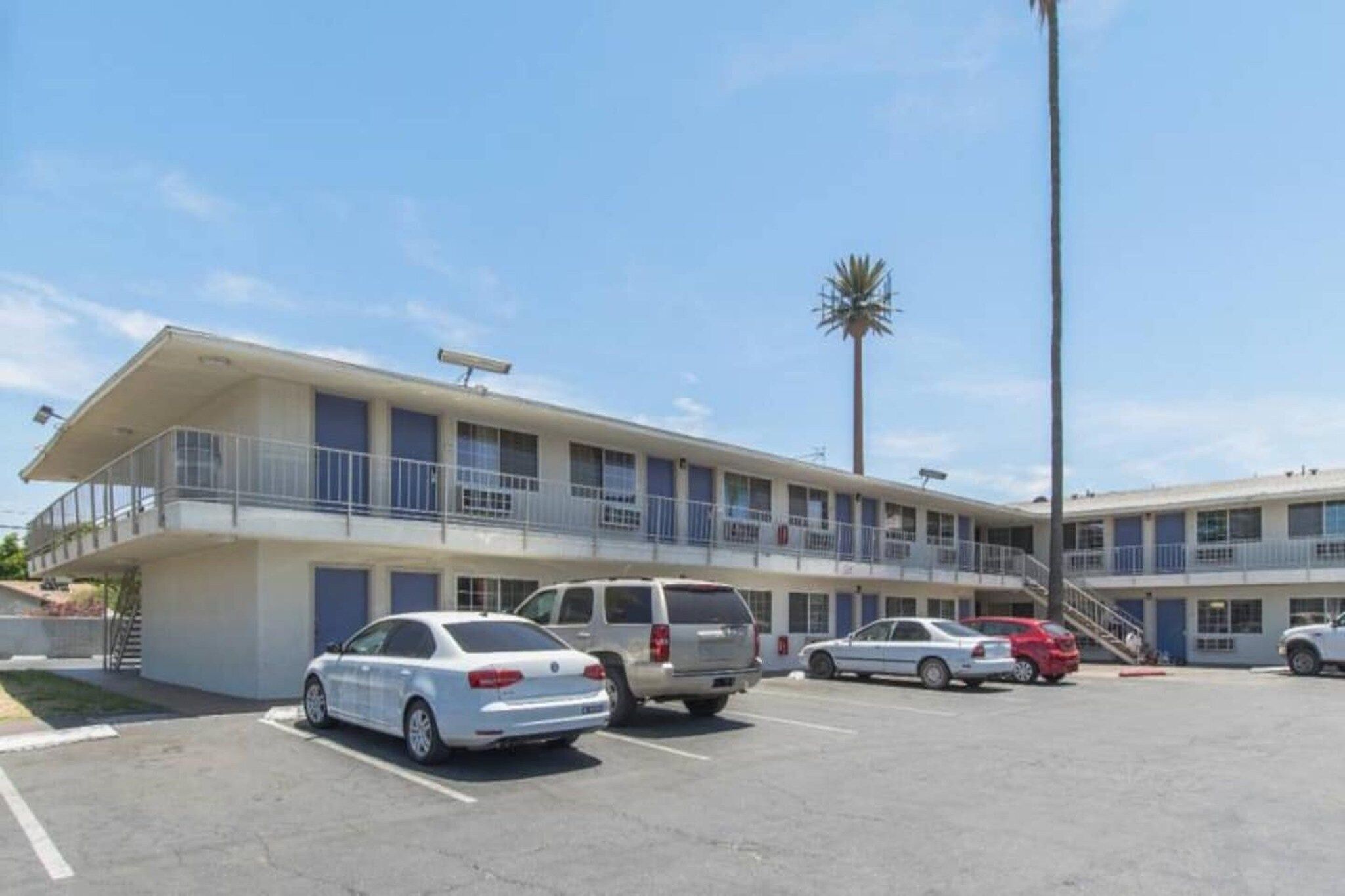 Ein Motel mit zweistöckigem Bau, einem Parkplatz mit mehreren Autos und einer Palme im Hintergrund.