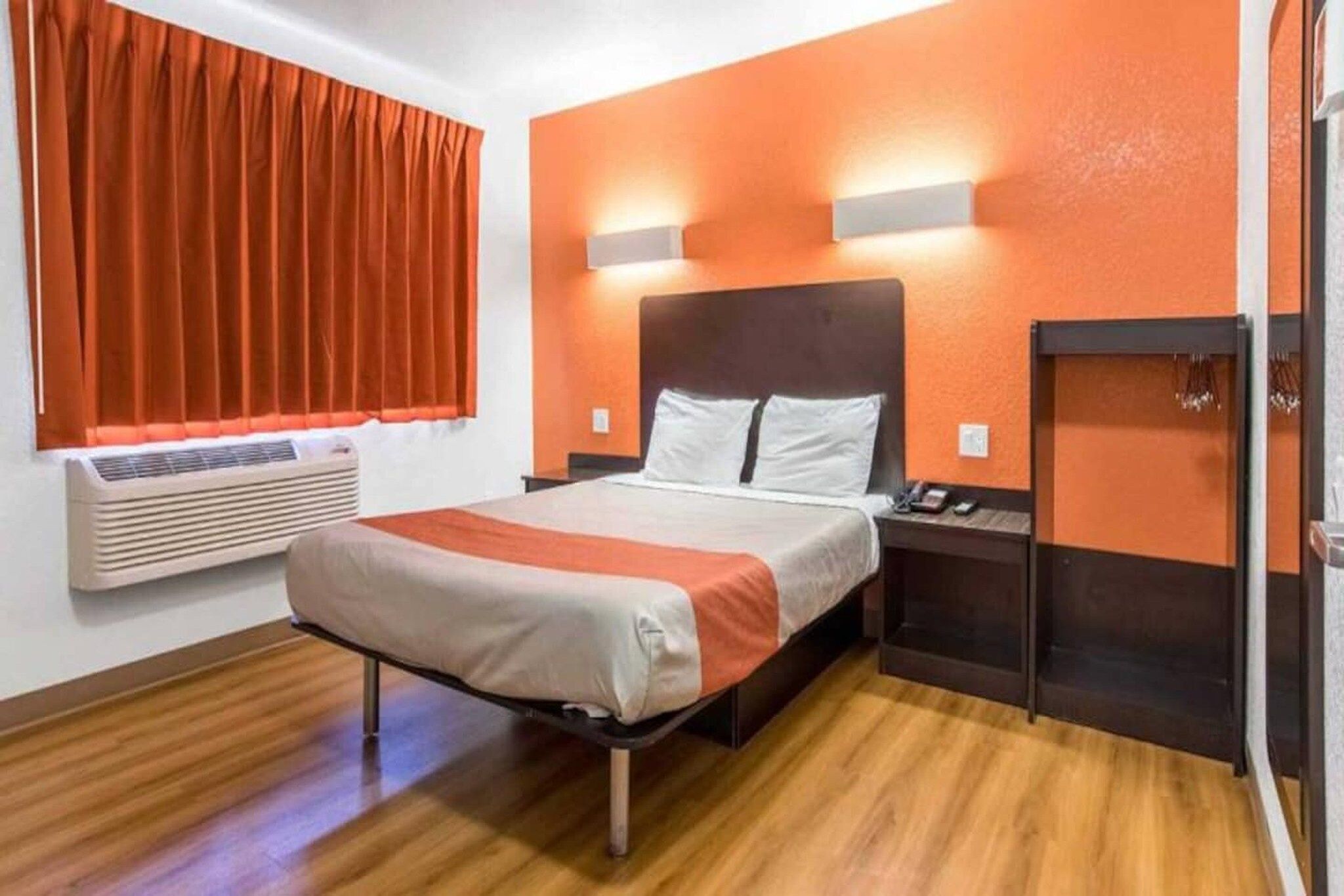 Habitación de hotel con una cama, mesita de noche, teléfono, calefacción y una ventana con cortinas.