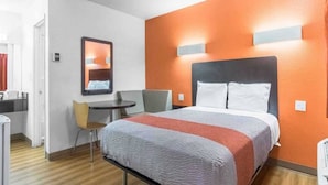 Ein Hotelzimmer mit Bett, Schreibtisch, Stuhl und Spiegel.