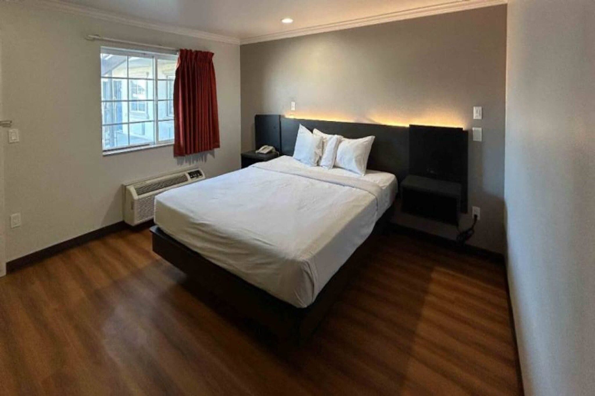 Une chambre d’hôtel avec un grand lit, une table de chevet, un radiateur, une fenêtre avec des rideaux et une lampe fixée au mur.