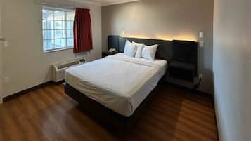 Une chambre d’hôtel avec un grand lit, une table de chevet, un radiateur, une fenêtre avec des rideaux et une lampe fixée au mur.