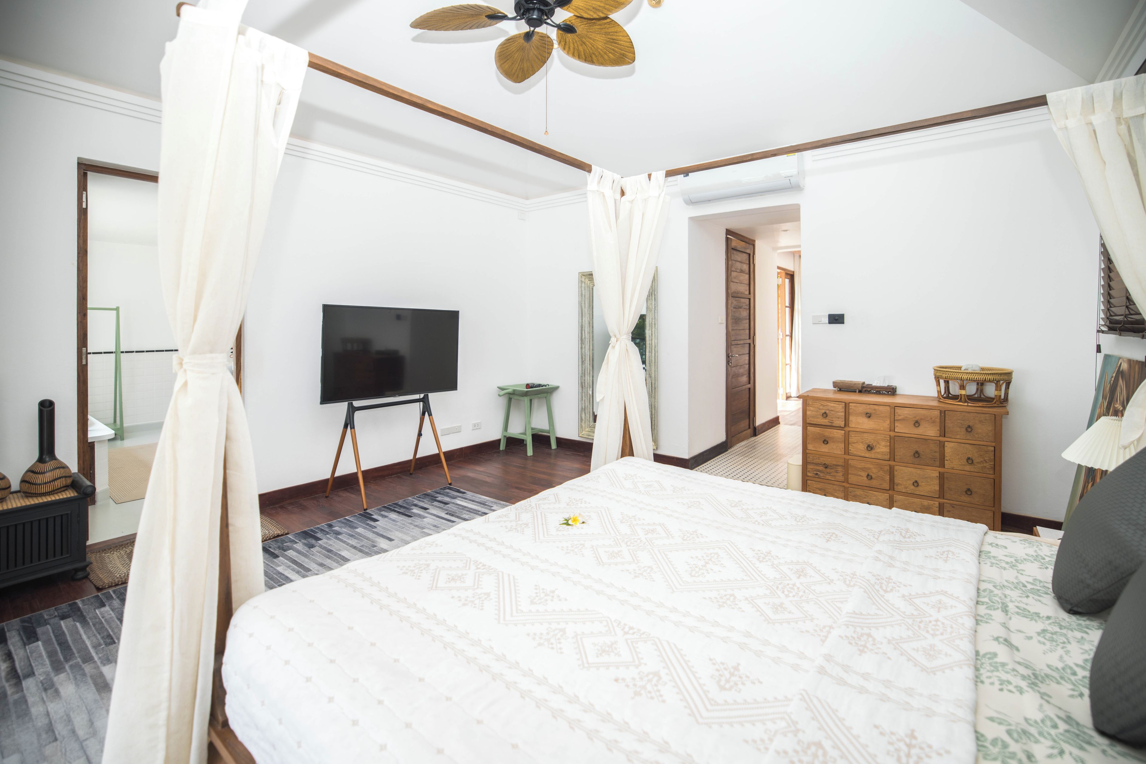 A bedroom with a large bed, a television, a wooden dresser, and a ceiling fan.