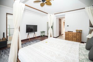 Un dormitorio con una cama grande, televisión, cómoda de madera y ventilador de techo.