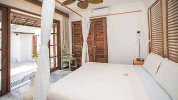 Un dormitorio con cama, contraventanas de madera, ventilador de techo y vista al exterior.