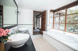 Une salle de bain moderne avec deux lavabos, une grande baignoire et une fenêtre donnant sur la verdure.