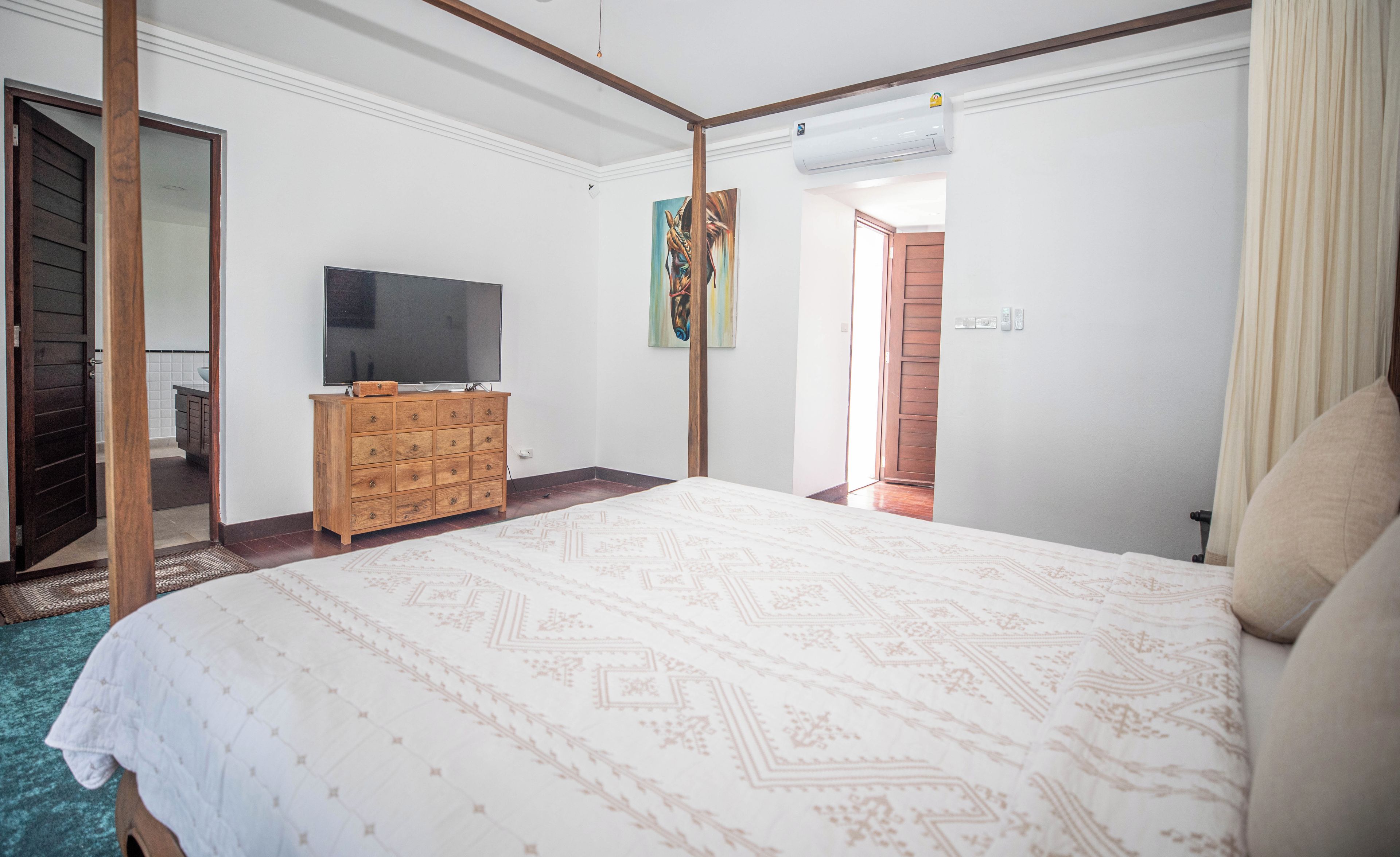 Un dormitorio con una cama grande, un aparador de madera, un televisor y un cuadro en la pared.
