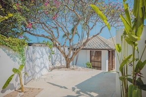 Un patio con un árbol, un edificio pequeño y un muro blanco.