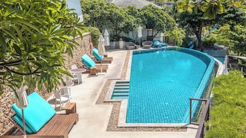 A swimming pool with lounge chairs and umbrellas, surrounded by greenery and a stone wall.