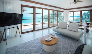 Un salón moderno con un televisor grande, un sofá, una mesa de centro y vistas al océano a través de amplias ventanas.