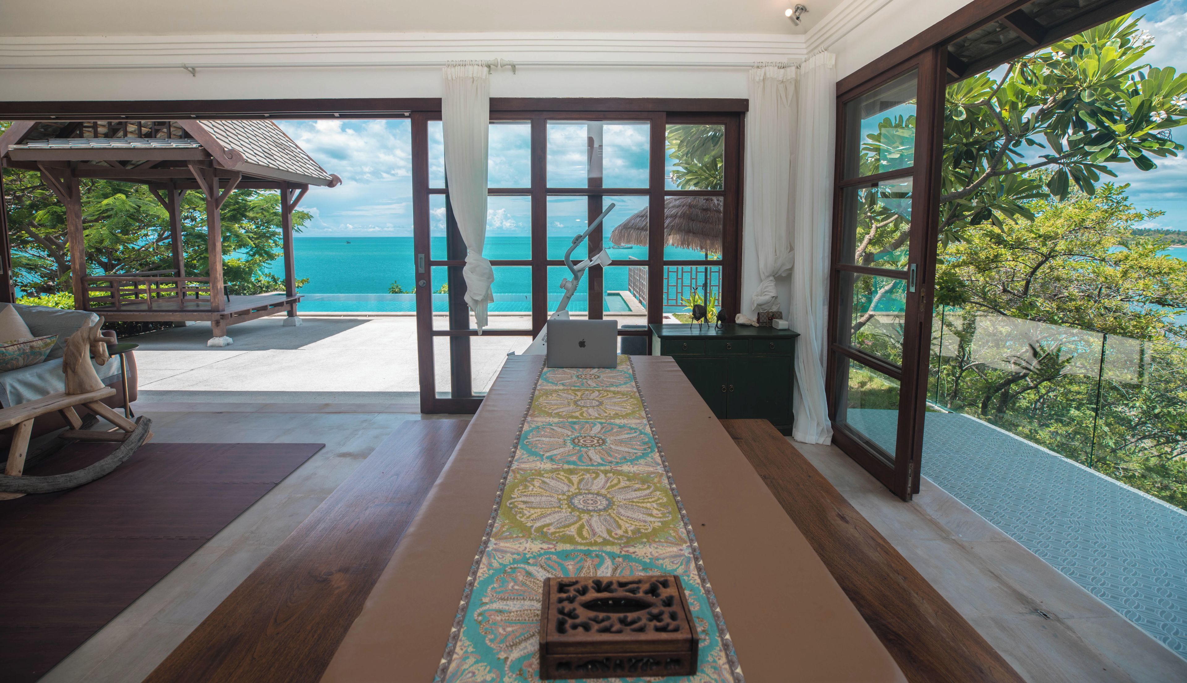 A room with a view of the ocean, a wooden table, a laptop, and a decorative box.