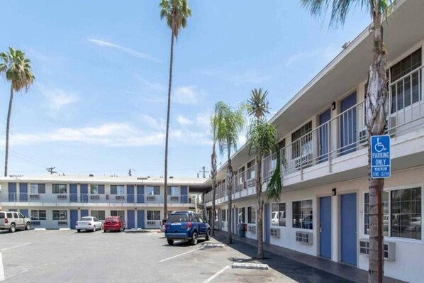 A motel with a parking lot, a blue handicapped parking sign, and palm trees.