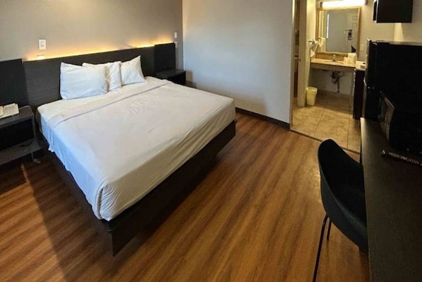 A hotel room with a large bed, a nightstand, a desk with a chair, and a bathroom visible through an open door.