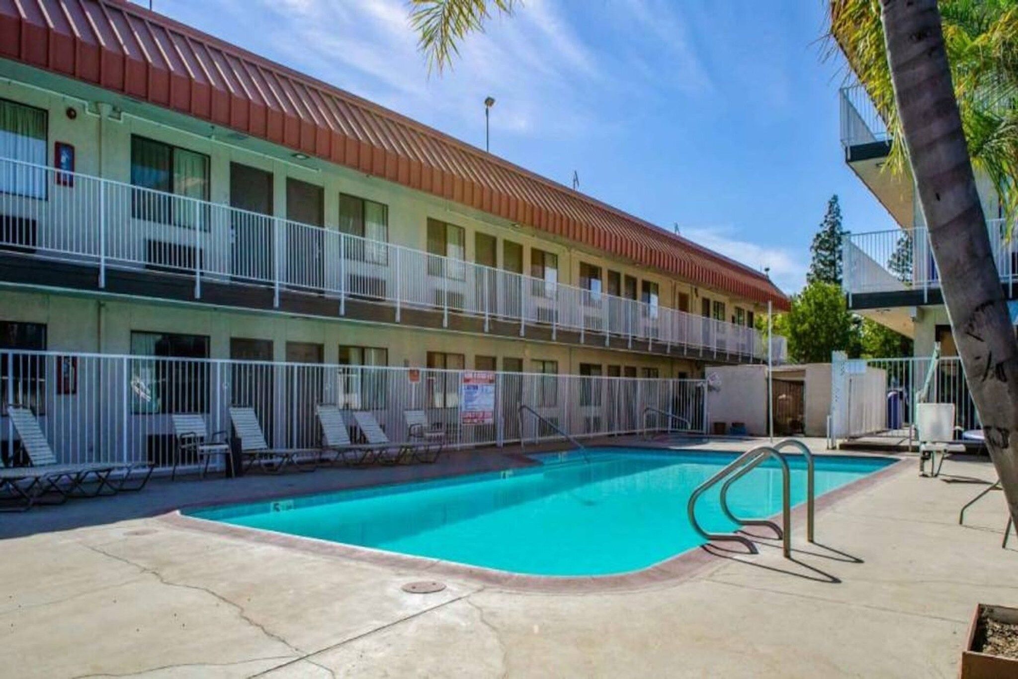 A motel with a swimming pool, a fenced deck area, and a two-story building with balconies.