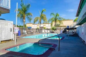 Área de piscina com trampolim, espreguiçadeiras e palmeiras ao fundo.