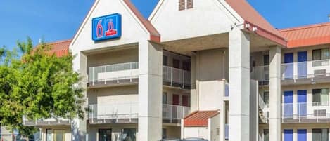 A hotel with a prominent '6' sign, multiple balconies, and a parking lot with cars.