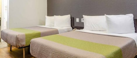 Two twin beds with a neutral color scheme, a wooden floor, and a plain wall.