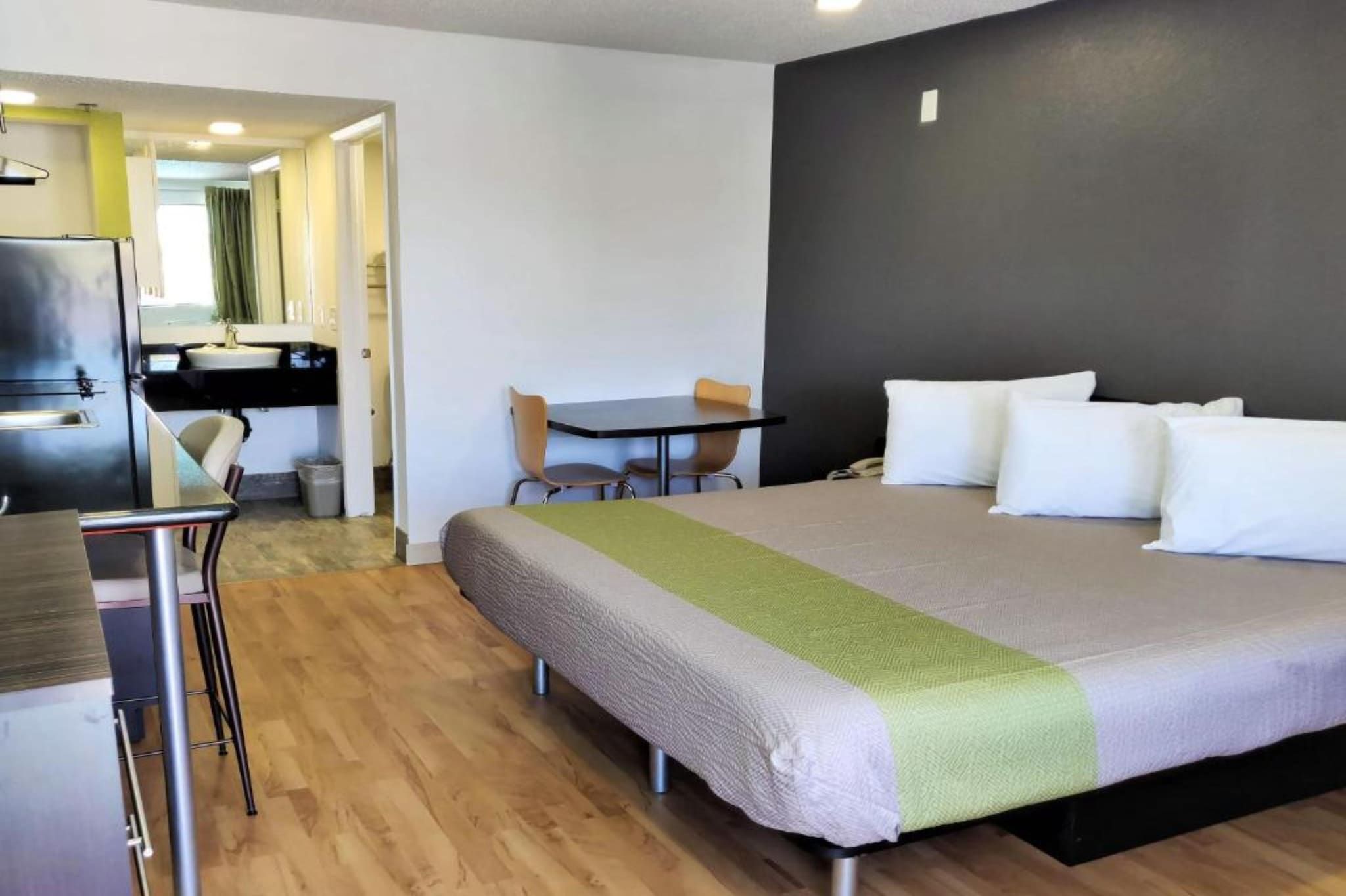 A hotel room with a bed, a desk, a chair, a small table, and a bathroom visible through an open door.