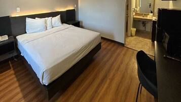 A hotel room with a large bed, a nightstand, a desk with a chair, and a bathroom visible through an open door.