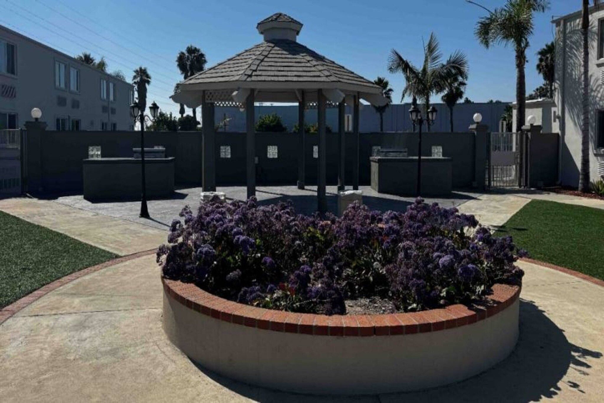 A gazebo with a circular flower bed in the center, surrounded by a low wall and a well-maintained lawn.
