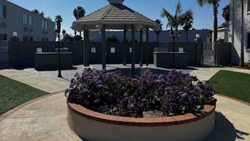 A gazebo with a circular flower bed in the center, surrounded by a low wall and a well-maintained lawn.