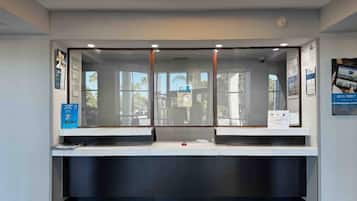 A reception desk with a glass partition, a computer monitor, and a sign on the wall.