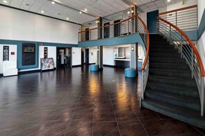 Un amplio espacio interior con piso de baldosas oscuras, una escalera con barandillas metálicas y un nivel superior con pasamanos.