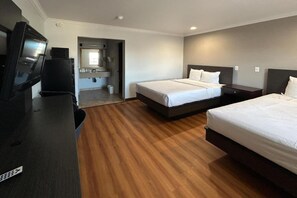 Habitación de hotel con dos camas, un televisor, un escritorio y un baño visible a través de una puerta abierta.