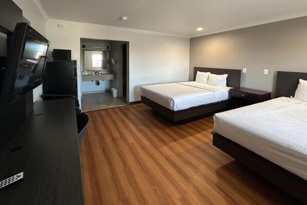A hotel room with two beds, a TV, a desk, and a bathroom visible through an open door.