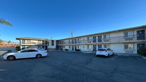 Um motel com dois carros estacionados na entrada, céu claro e um poste de eletricidade.