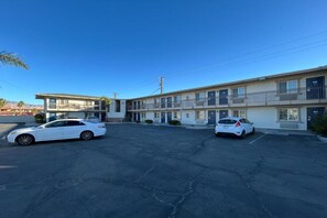 Un motel con dos autos estacionados en la entrada, cielo despejado y un poste de servicios.