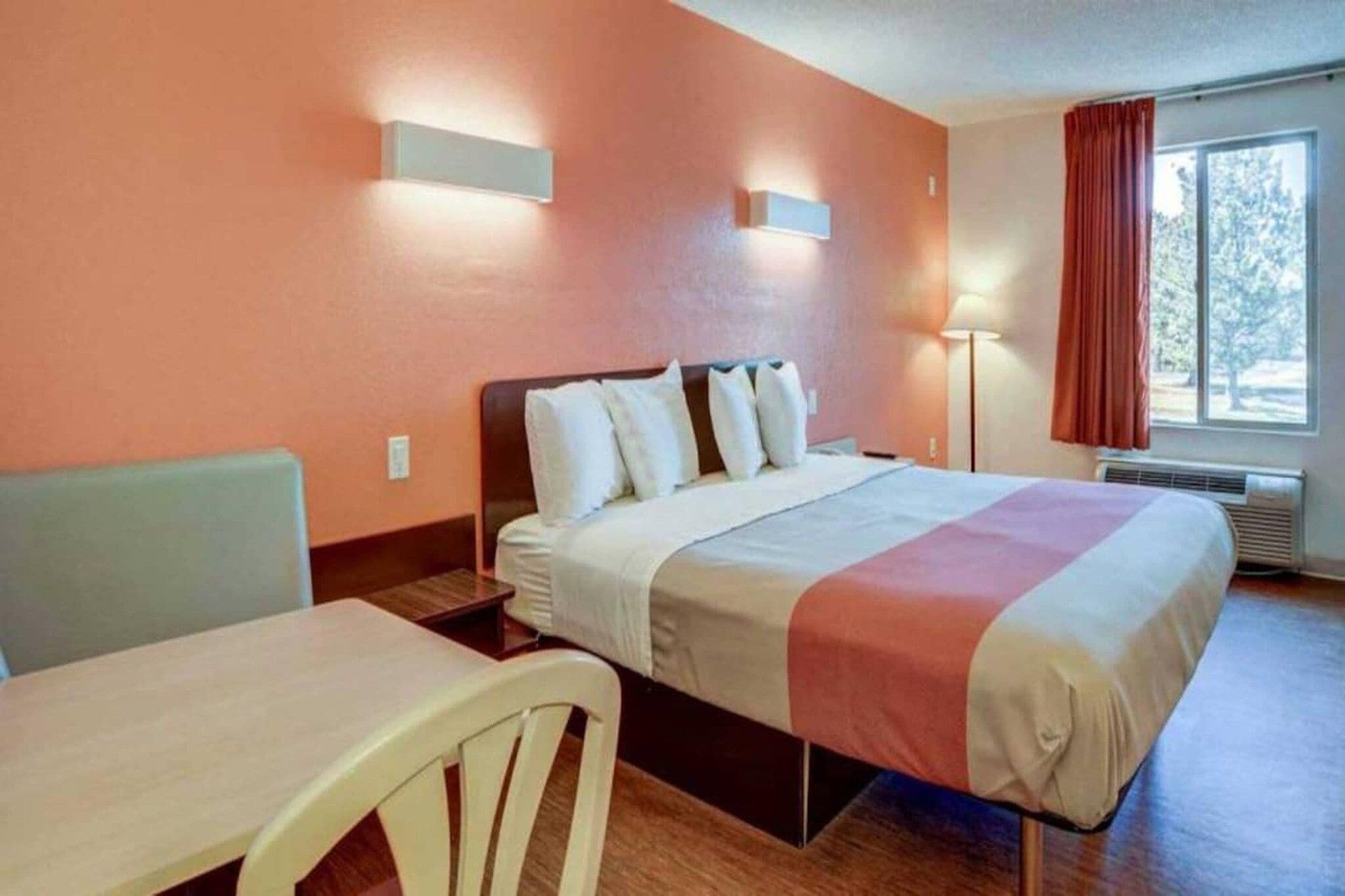 A hotel room with a bed, a desk, a chair, a nightstand, and a window with curtains.