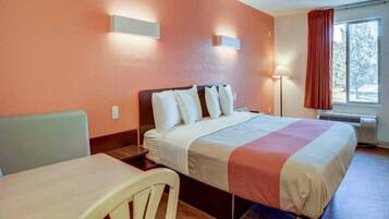 A hotel room with a bed, a desk, a chair, a nightstand, and a window with curtains.