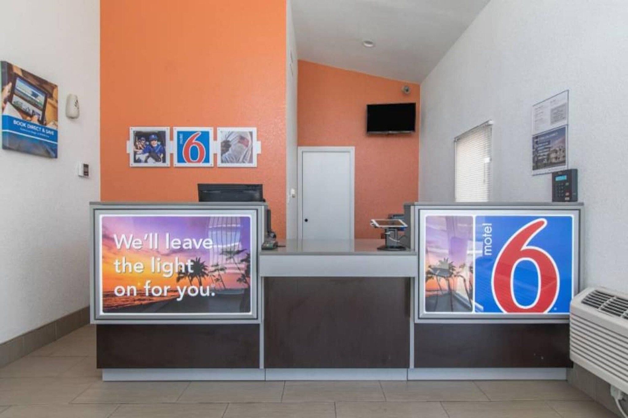 Un mostrador de recepción de hotel con un cartel grande con el número '6', una pantalla digital mostrando un mensaje y una puerta al fondo.