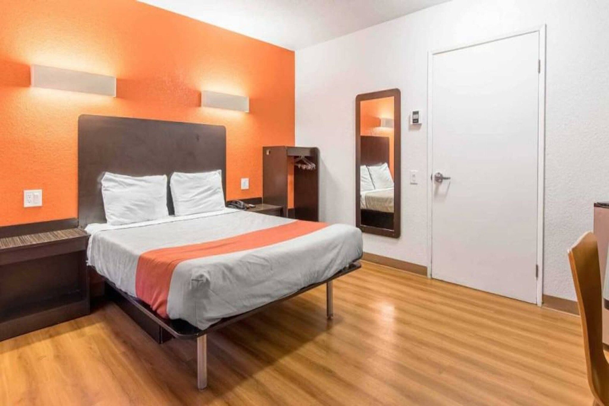 Una habitación de hotel con cama, mesita de noche, espejo y puerta.