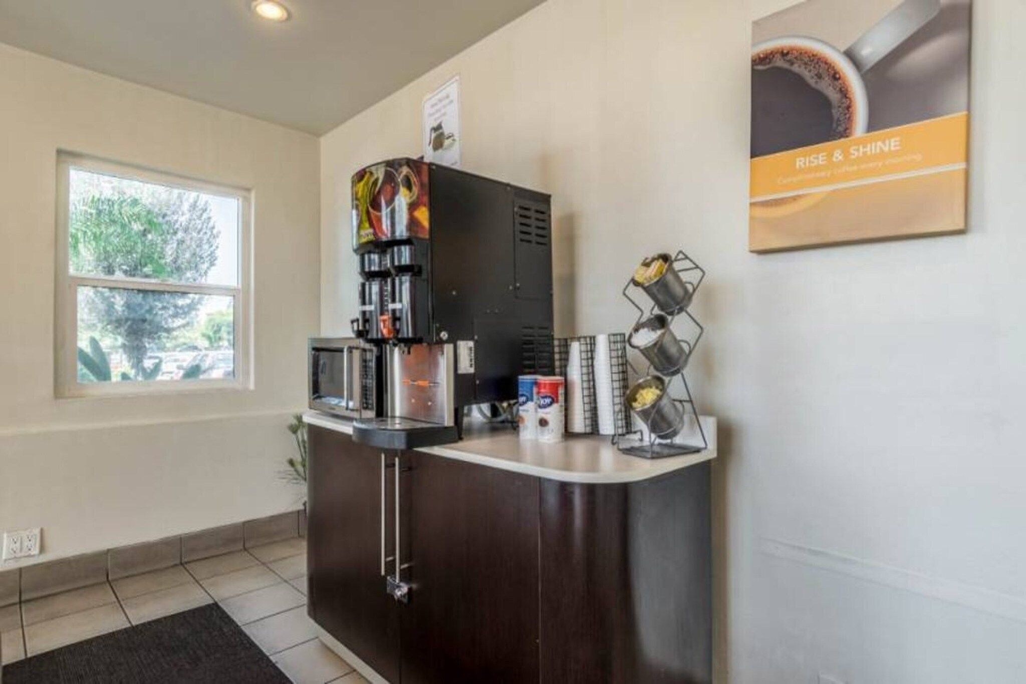 Zona de recepción con cafetera, microondas y refrigerador pequeño. Se ve una ventana con vista a árboles.