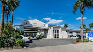 A motel with a covered parking area, palm trees, and a clear blue sky. - Redlands, Ca 2 QUEEN BEDS | SMK (REDLANDS)