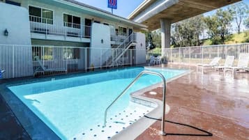 A swimming pool with a metal ladder, a covered area, and a building with a sign indicating a room number.