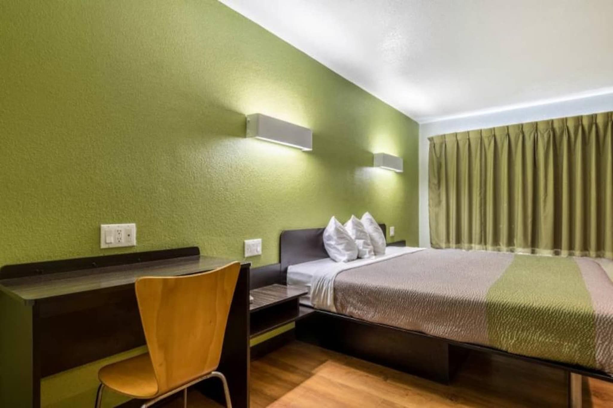 Habitación de hotel con cama, escritorio, silla y ventana con cortinas.