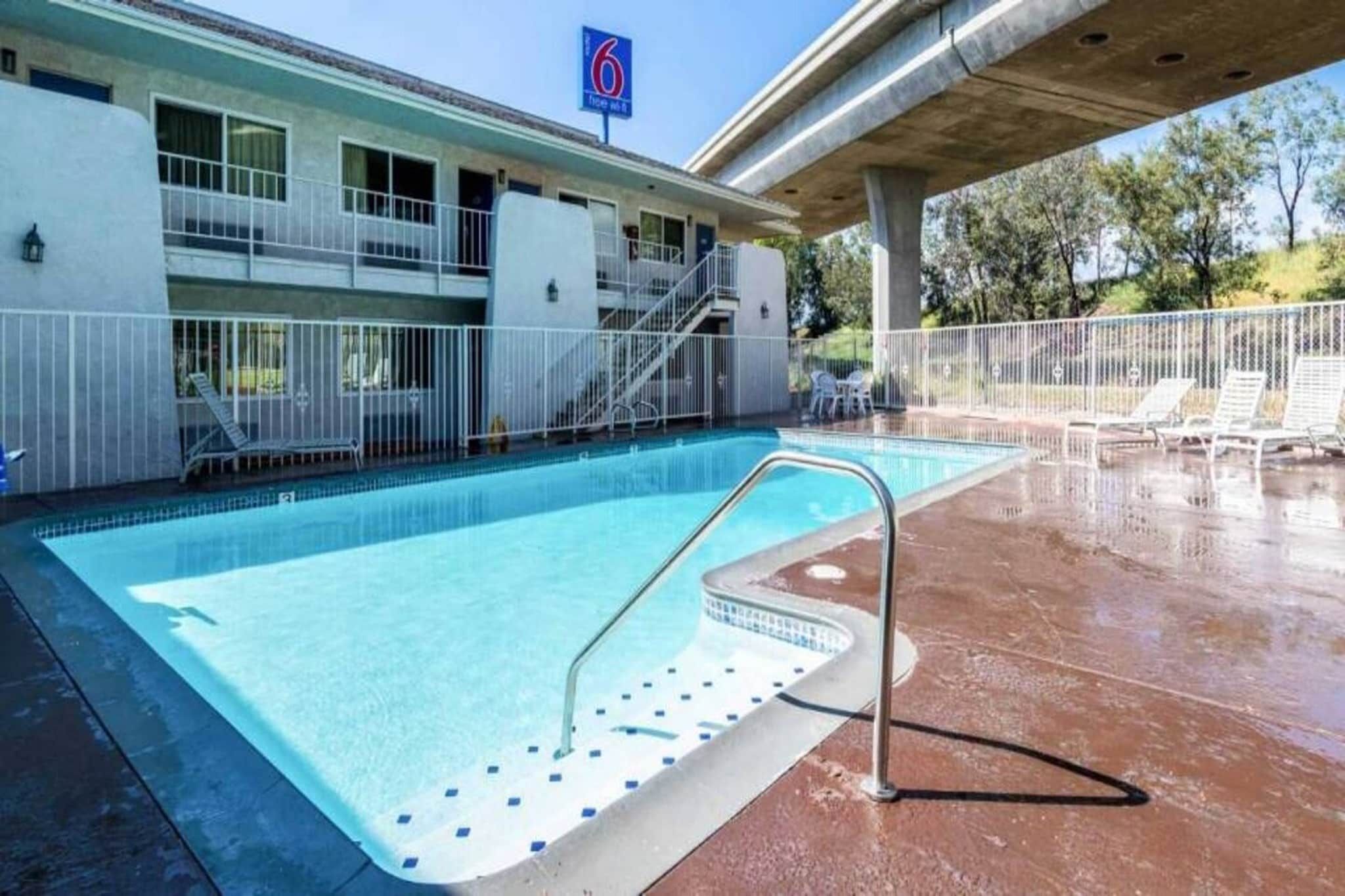 Una piscina con una escalera de metal, una zona cubierta y un edificio con un letrero que indica un número de habitación.