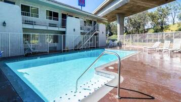 Una piscina con una escalera de metal, una zona cubierta y un edificio con un letrero que indica un número de habitación.
