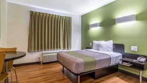 Una camera d'albergo con un letto, un comodino, una sedia e una finestra con tende.
