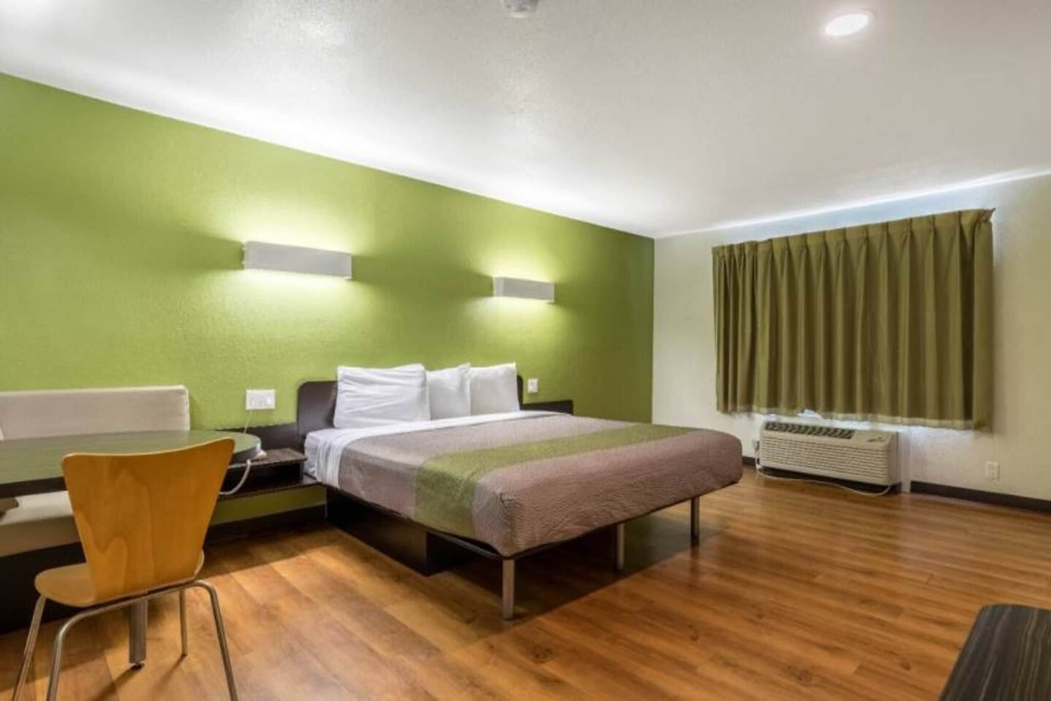 A hotel room with a bed, a desk, a chair, and a window with curtains.
