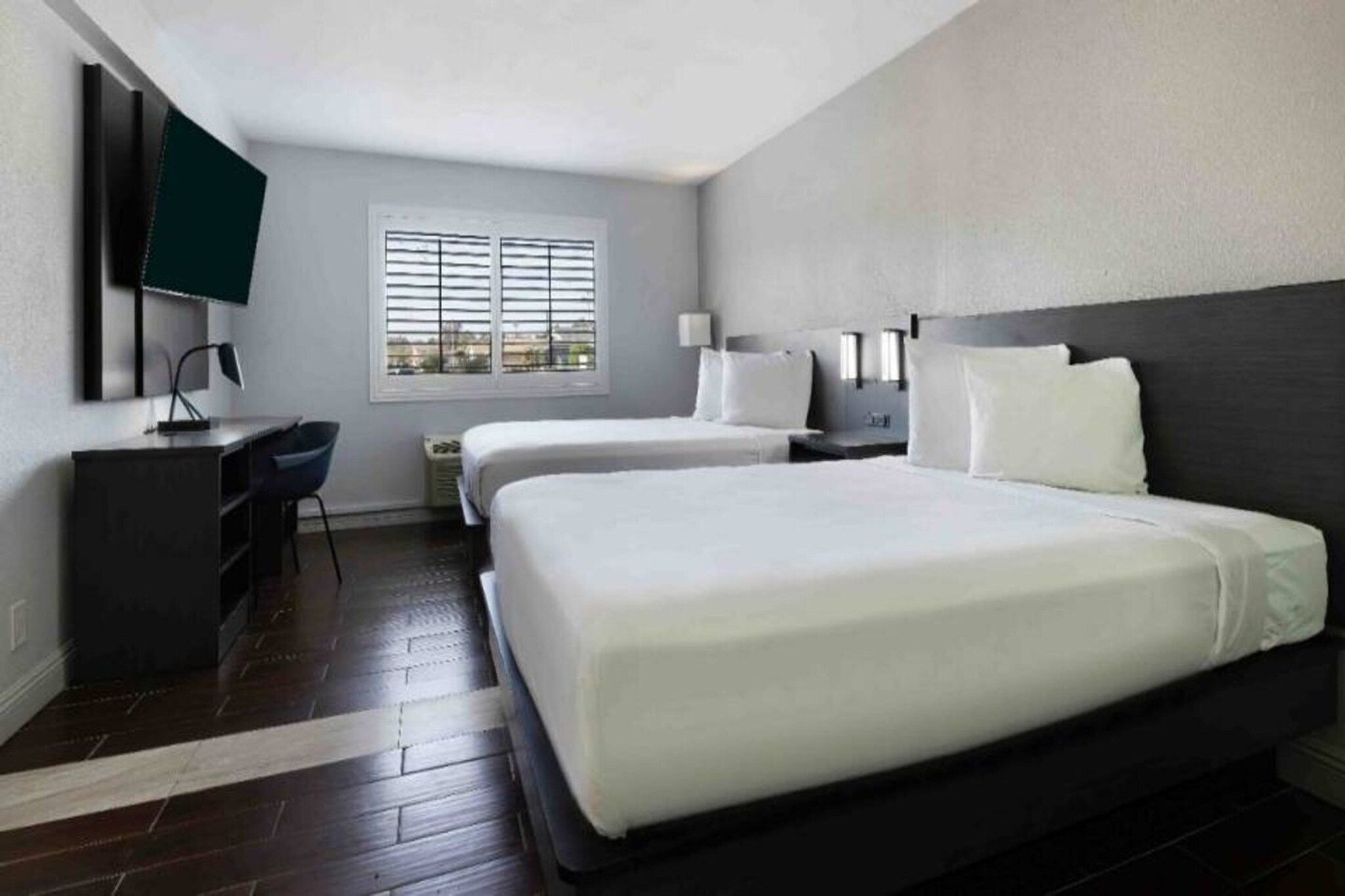 Une chambre d’hôtel avec un grand lit, un bureau, une chaise, une télévision et une fenêtre avec des stores.