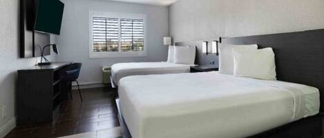 A hotel room with a large bed, a desk, a chair, a TV, and a window with blinds.
