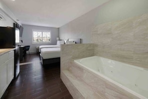 A modern bathroom with a large bathtub, a shower area, and a separate bedroom with a bed and a desk. - 1 King - 2 Queen Beds | Non-Smoking, Kitchen (Artesia)