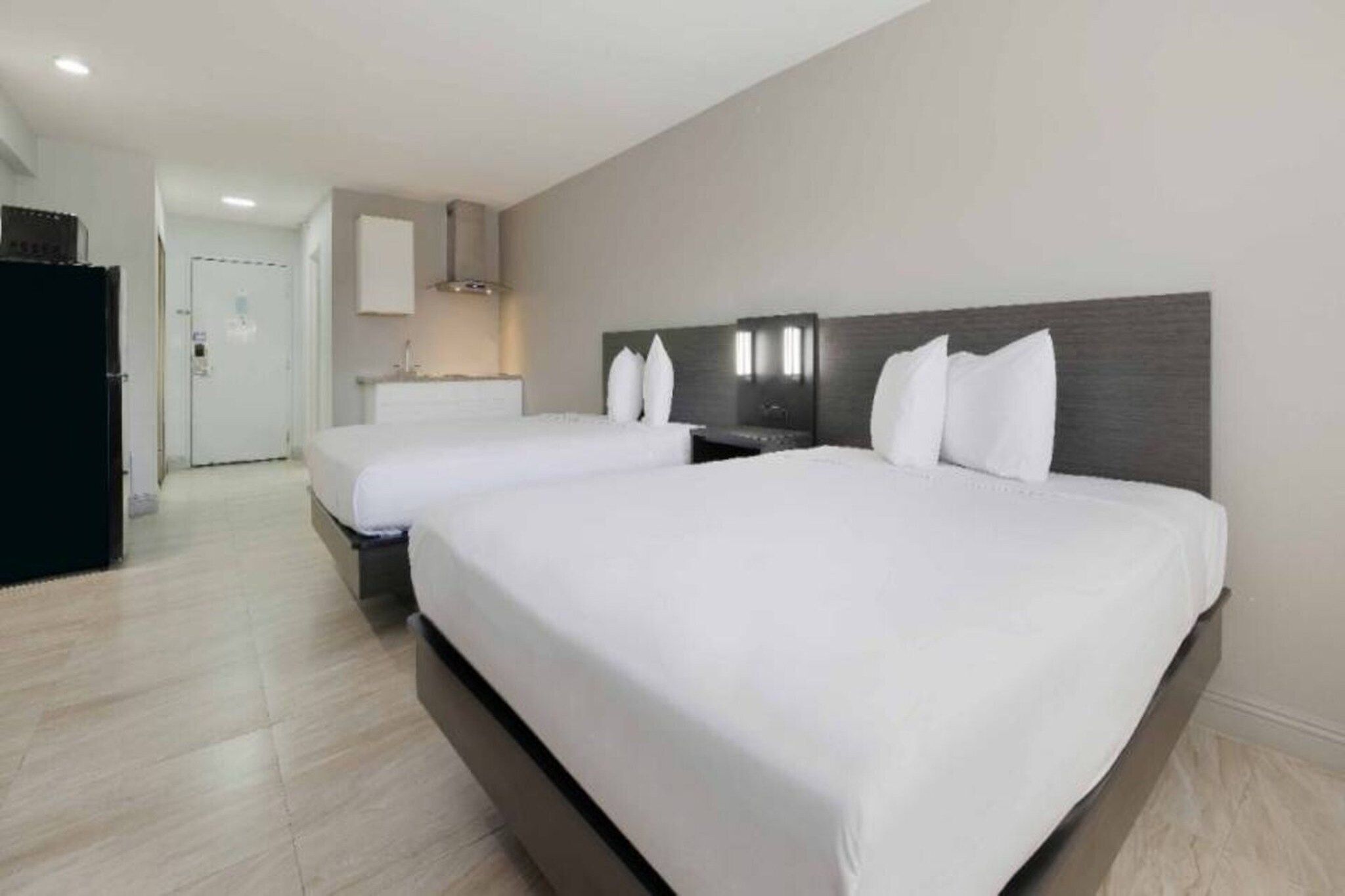 A hotel room with two beds, a kitchenette, and a bathroom.