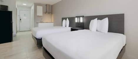 A hotel room with two beds, a kitchenette, and a bathroom.